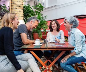 A group of 4 adults laughing together, sitting around a table with coffee