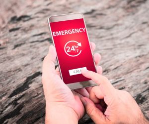 Hands holding a mobile phone with emergency at top of red screen and finger about to hit call button