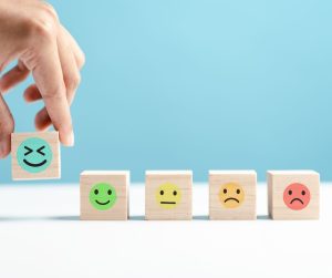 a hand placing a wooden block in a row of blocks with different faces printed on them from laughing to sad