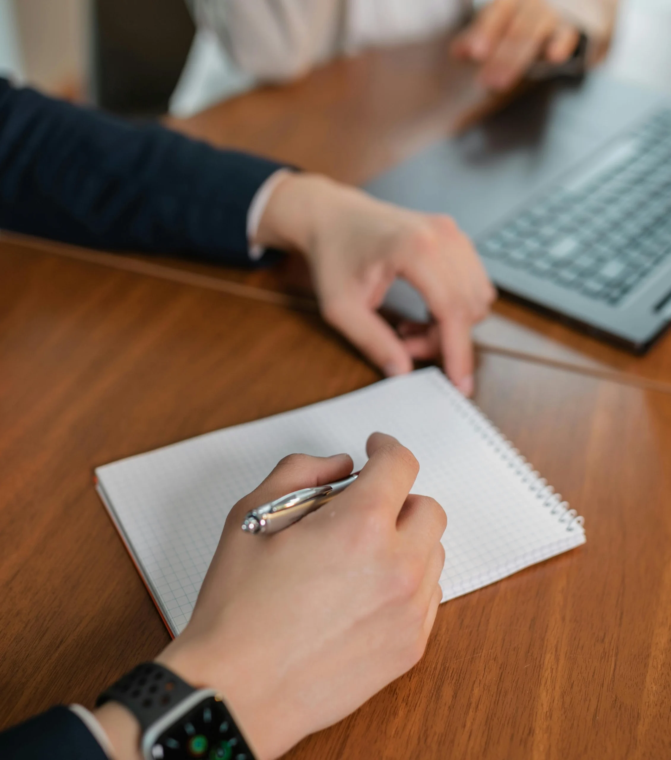 a hand holding a pen hovering over a piece of paper on a wooden desk