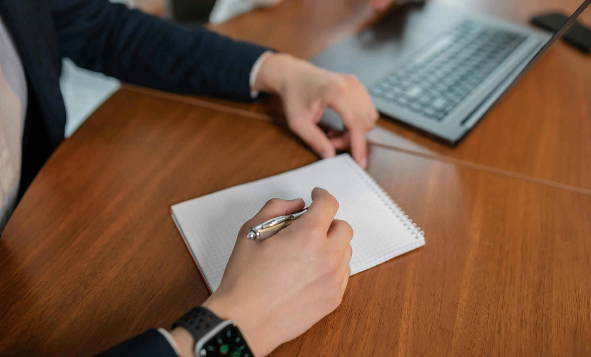 a hand holding a pen hovering over a piece of paper on a wooden desk