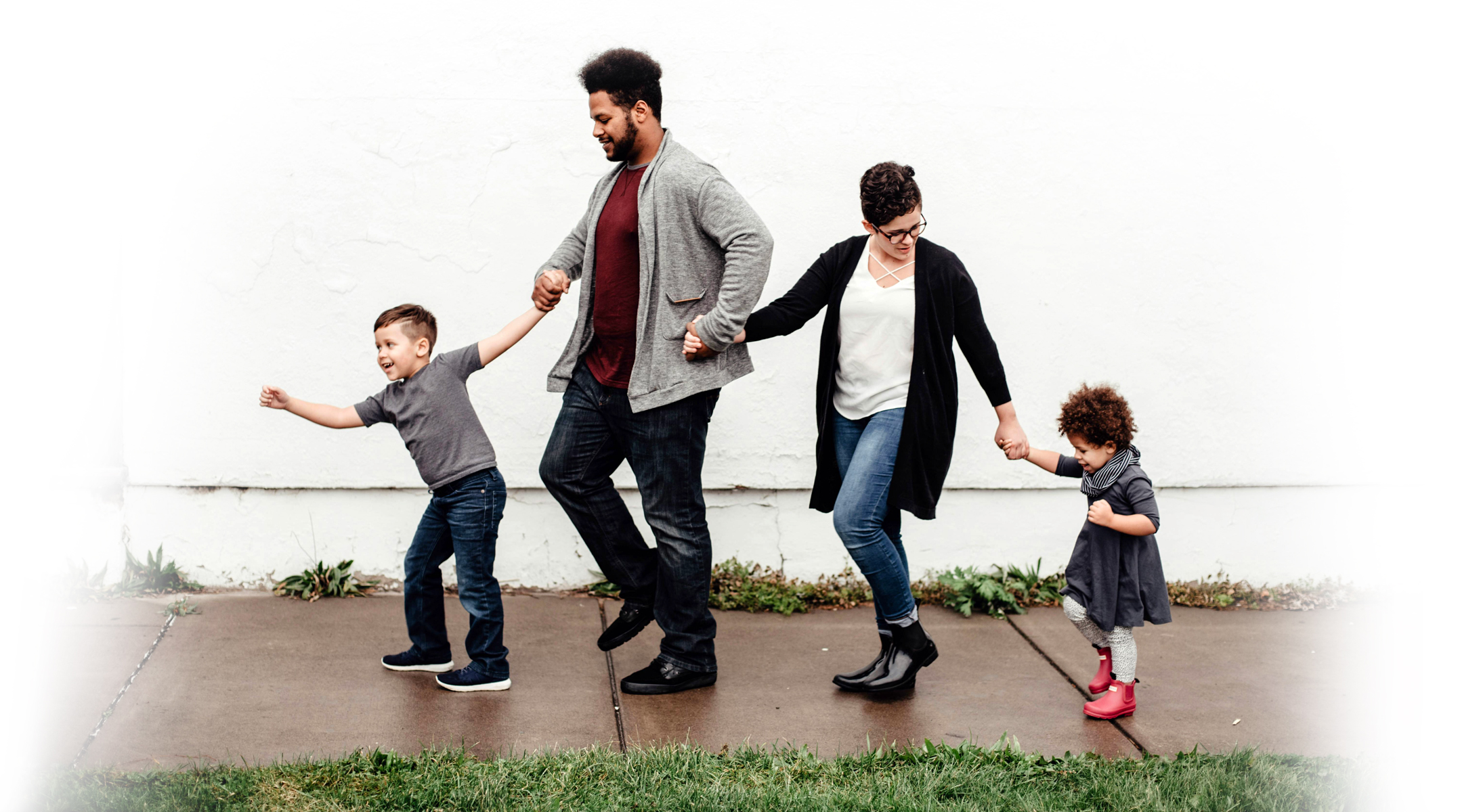 Mixed race family with parents and 2 children all holding hands walking down a path
