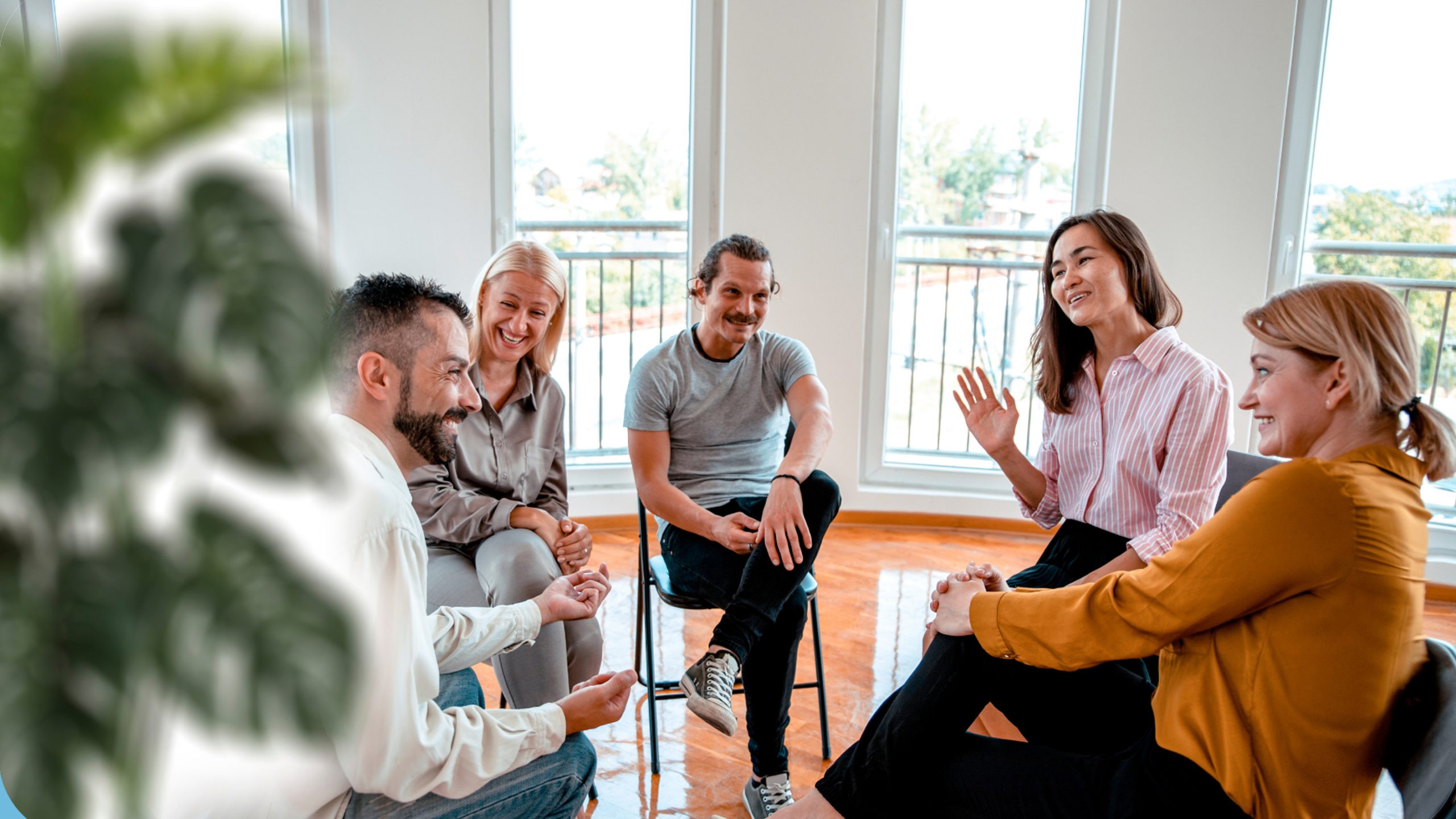 A group of 5 adults sitting in a room facing each other talking and laughing